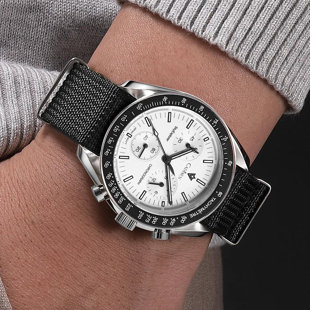 Close-up of wrist wearing a black strap wristwatch with white chronograph dial and tachymeter bezel
