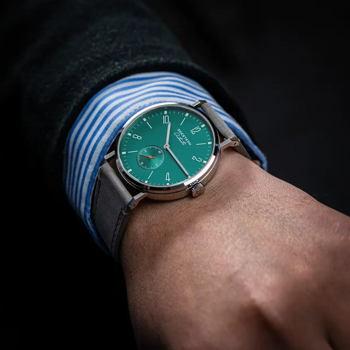 Close-up of wrist wearing a green dial SESTERN wristwatch with silver case and grey leather strap